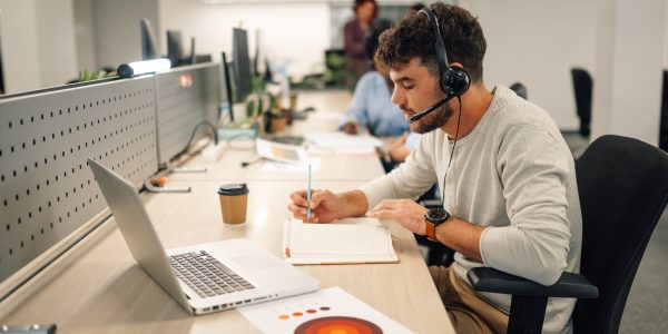 customer-services-agent-with-headset-writing-notes-in-a-call-center-1.jpg